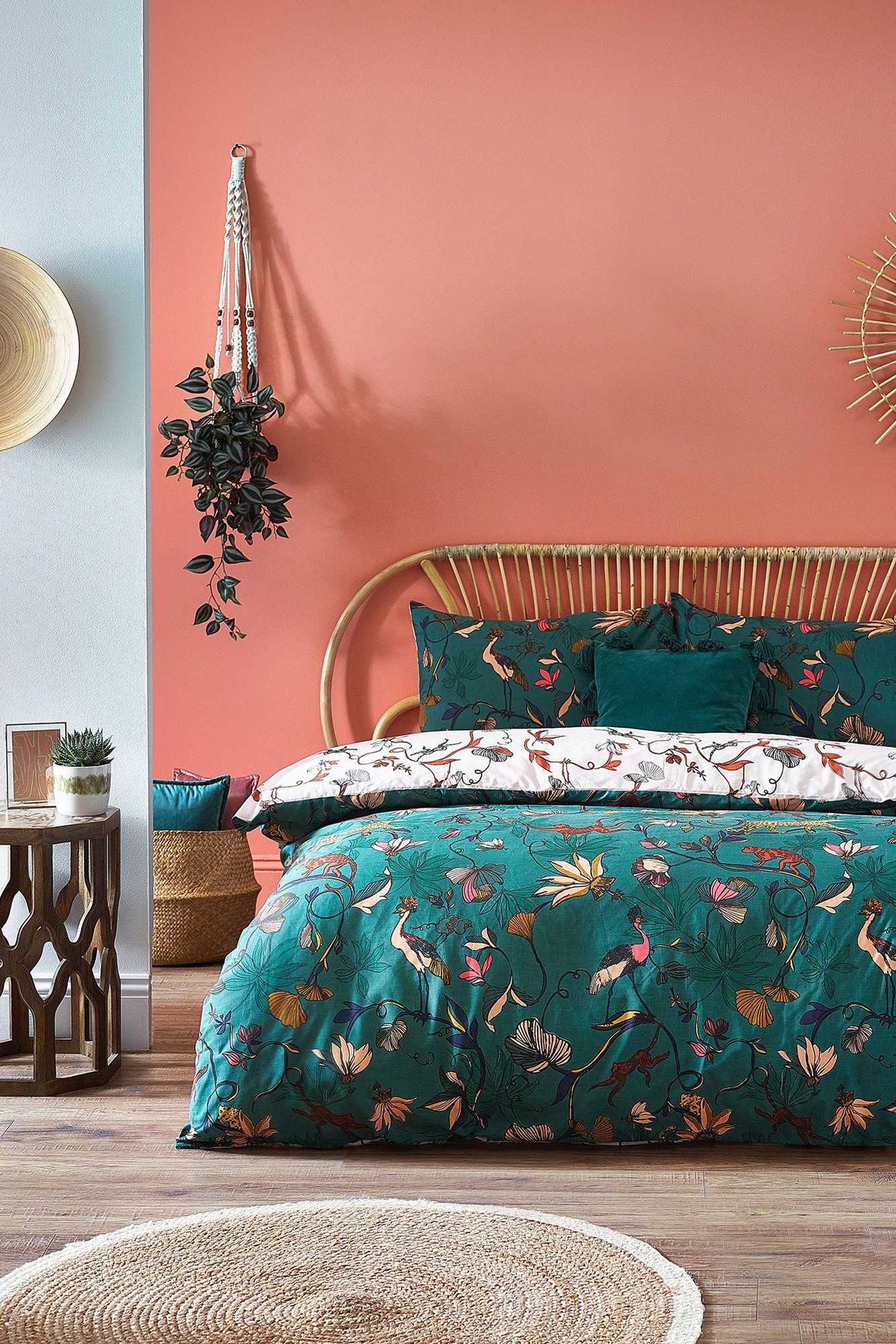 Green cotton duvet cover set featuring vibrant floral and bird patterns, paired with matching pillows, styled on a rattan bed against a coral wall with decorative elements.