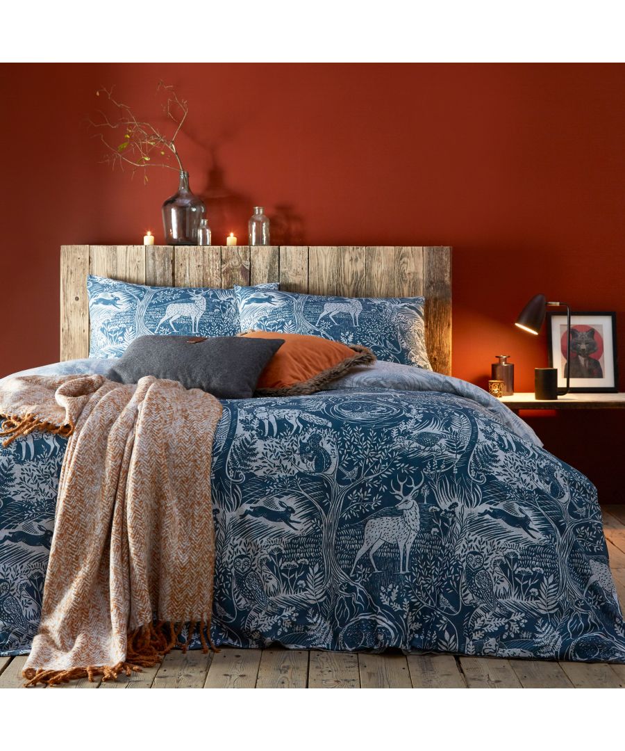 Midnight blue duvet set featuring a winter woods design with deer and foliage, complemented by textured cushions and a cozy throw, styled against a warm red wall.