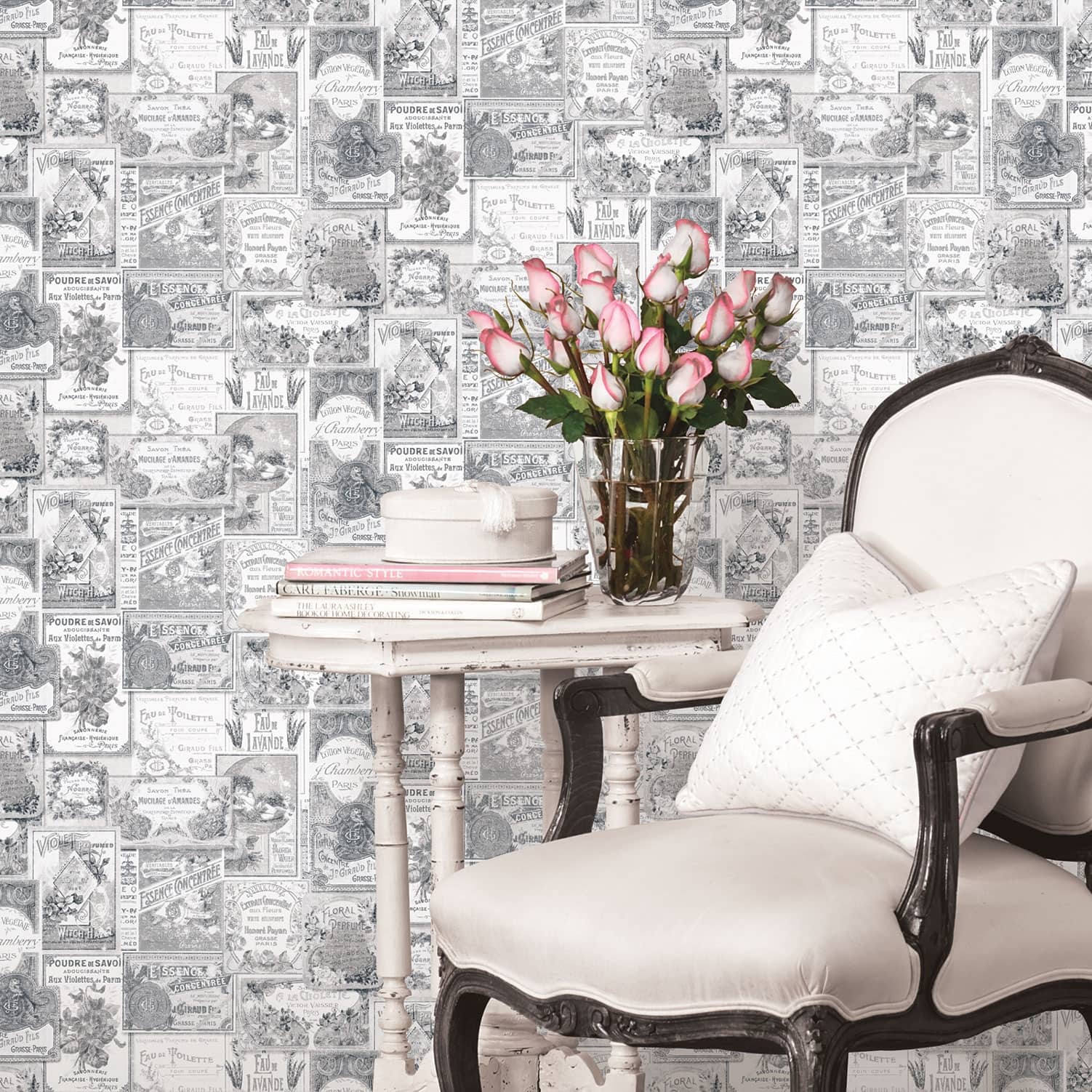 Nostalgie Perfume Labels Wallpaper features vintage-style illustrations in black and white, showcasing intricate designs, with a soft, elegant chair and a vase of pink roses in the foreground.