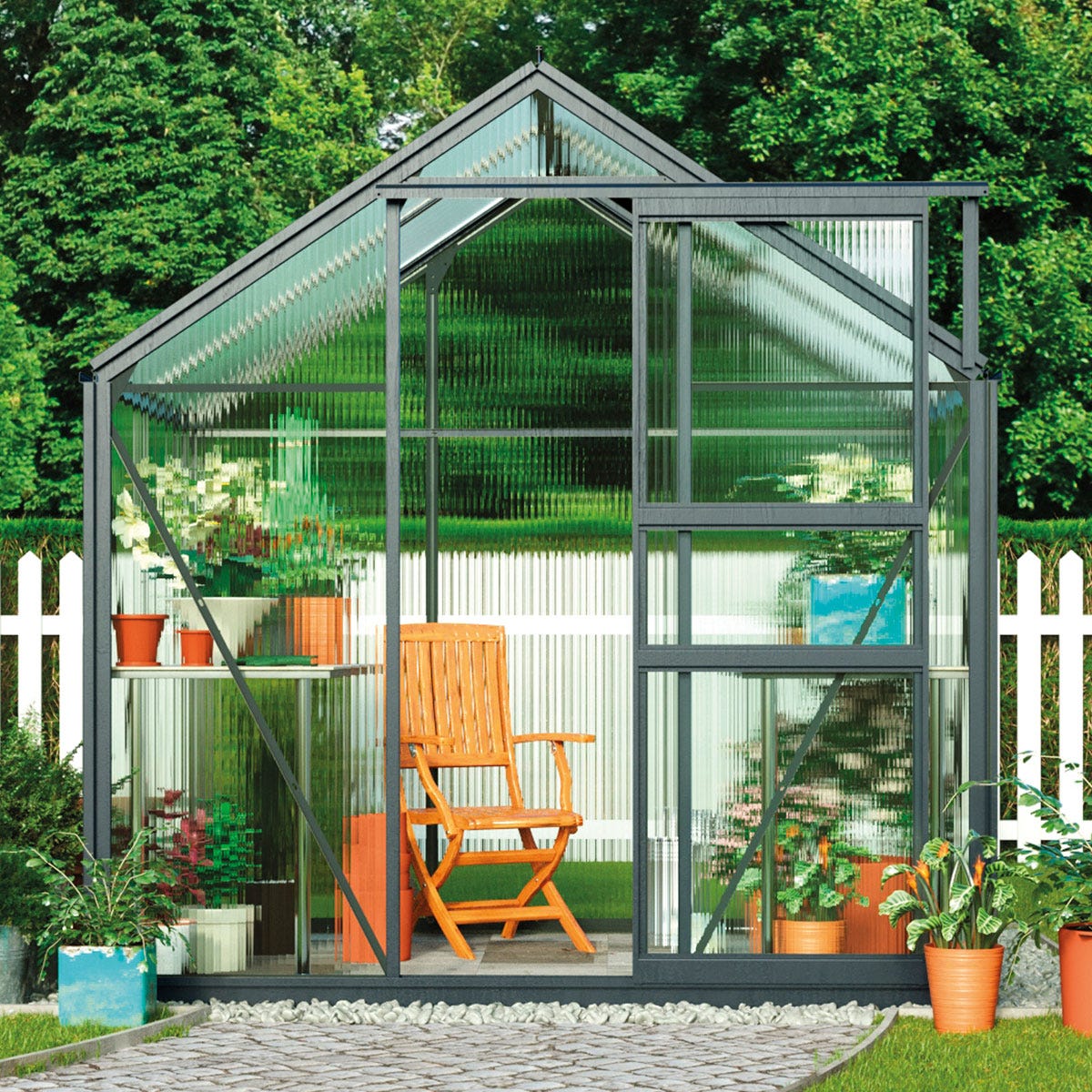 Garden Gear greenhouse measuring 6.2 x 4.3 x 6.6ft in grey, featuring a sturdy frame, transparent panels, and potted plants, with a wooden chair visible inside.