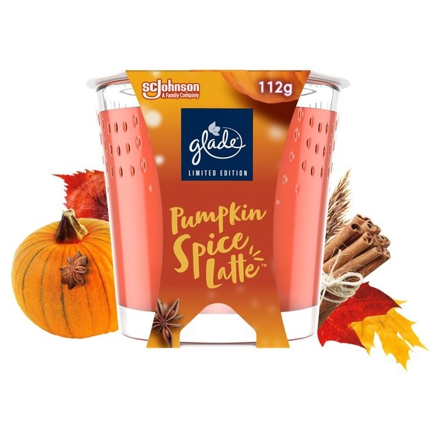 Glade's limited edition Pumpkin Spiced Latte scented candle in a clear glass holder, featuring orange hues, autumn leaves, a pumpkin, and cinnamon sticks.