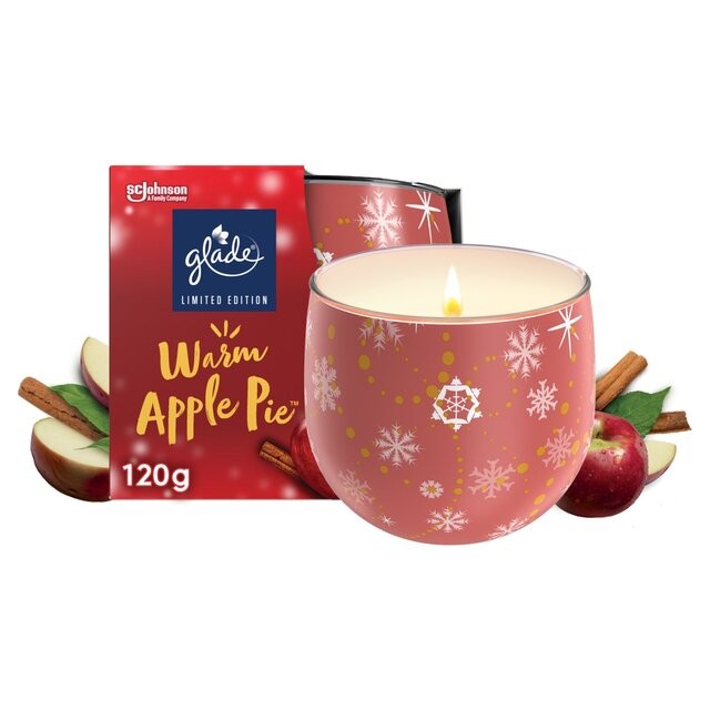 Pink glass candle holder with snowflake designs, filled with creamy wax, accompanied by a red box labeled "Warm Apple Pie," featuring apples and cinnamon sticks.
