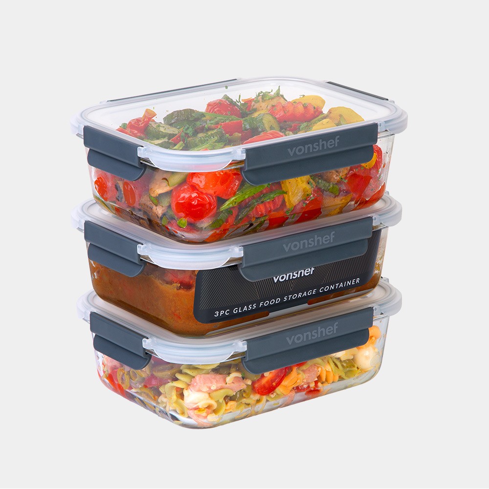 Three stackable glass food storage containers by VonHaus, featuring clear glass bodies, black silicone seals, and snap-lock lids, filled with colorful cooked vegetables and meats.
