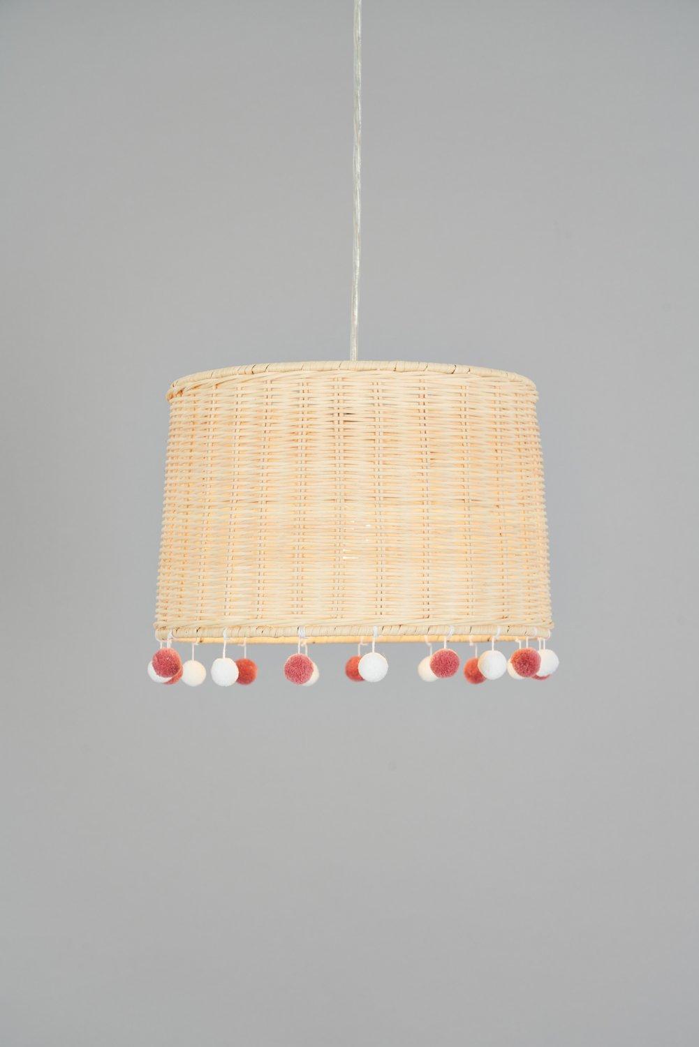 Natural rattan pendant shade featuring a cylindrical shape, adorned with colorful pom poms in red and white along the bottom edge, suspended by a clear cord.
