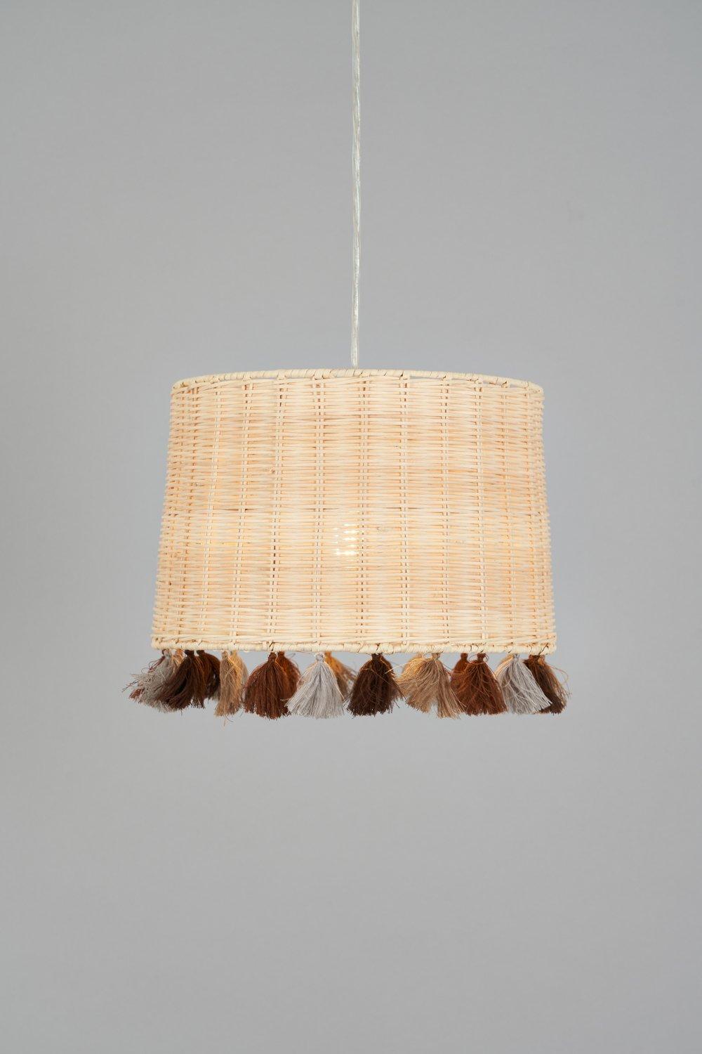 Natural rattan pendant shade featuring a cylindrical design with decorative tassels in brown, gray, and cream along the bottom edge.