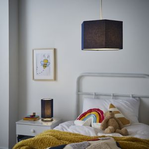 Silver hexagon table lamp with a sleek design, featuring a warm glow, set on a bedside table beside a cozy bed adorned with colorful pillows and a teddy bear.