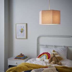 Pink hexagon light shade made of fabric, featuring a simple design, suspended from a cord in a cozy bedroom setting with a bed, colorful blanket, and framed artwork.