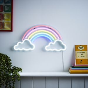 A colorful neon wall light featuring a rainbow with pastel pink, blue, and yellow arcs, flanked by two white cloud shapes, mounted on a wall above a shelf with books.