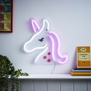 Multicoloured neon wall light shaped like a unicorn, featuring pink and purple glow, with a white outline and red stars, mounted on a white wall beside colorful books.