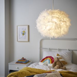 Large white feather light shade with a round shape, softly illuminated, hanging above a bed adorned with colorful blankets and a framed bee illustration on the wall.