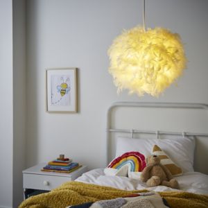 Yellow feather light shade hanging from the ceiling, casting a warm glow, above a cozy bed with a rainbow blanket, teddy bear, and colorful books on a nightstand.