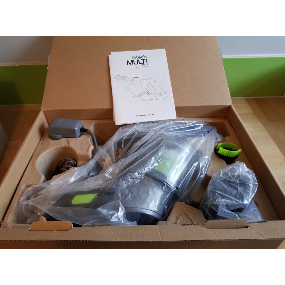 GTECH Multi Handheld Vacuum Cleaner in grey and green, featuring a sleek design, multiple attachments, and a user manual, all neatly packed in a cardboard box.