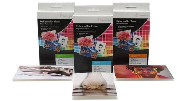 Three boxes of Hahnemühle Photo Matt Fibre paper in 10cm x 15cm size, featuring colorful designs, with sample prints showcasing vibrant images of flowers, a duck, and a portrait.