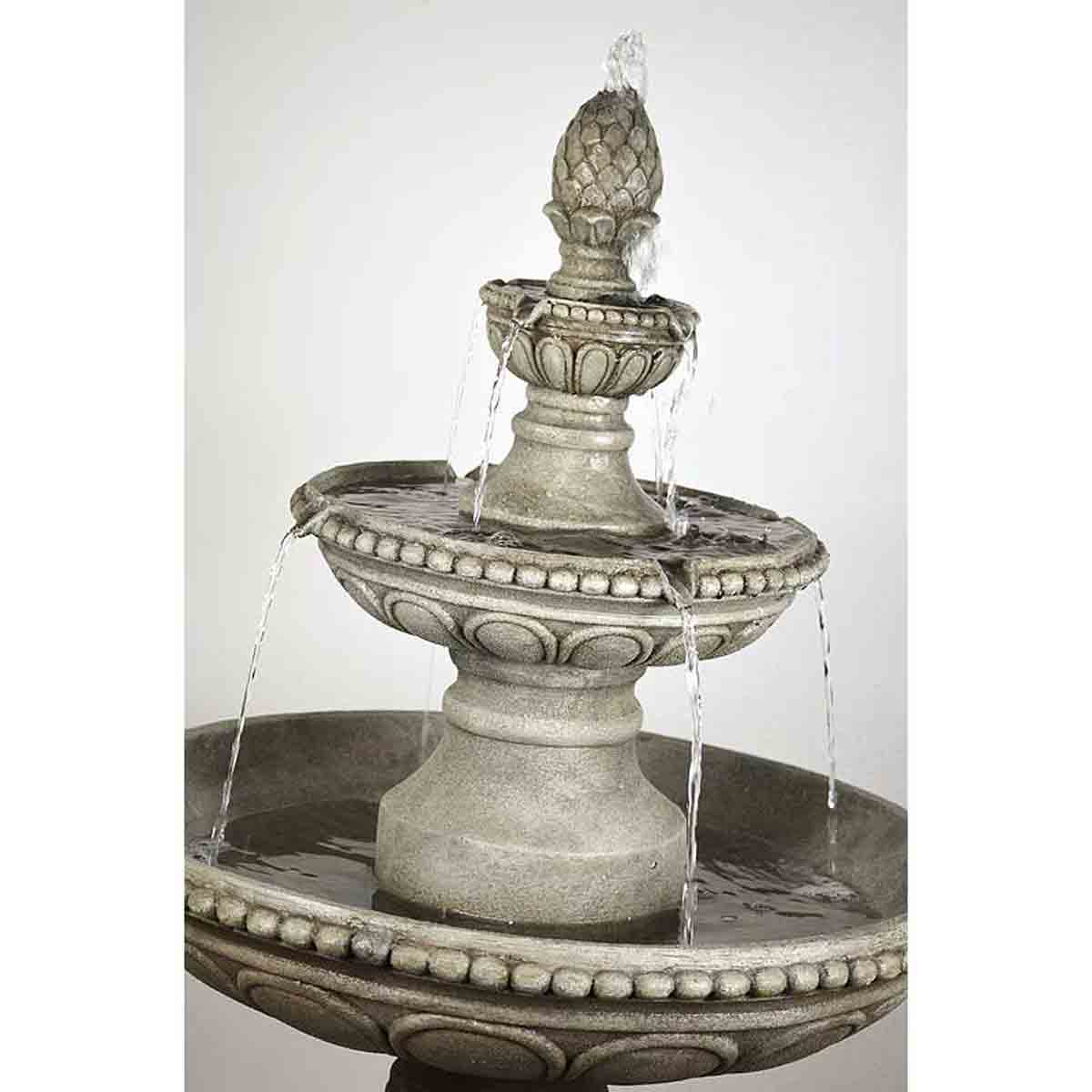 Three-tiered fountain in a stone-like finish, featuring ornate detailing and a decorative finial, with water cascading from each tier into the basin below.