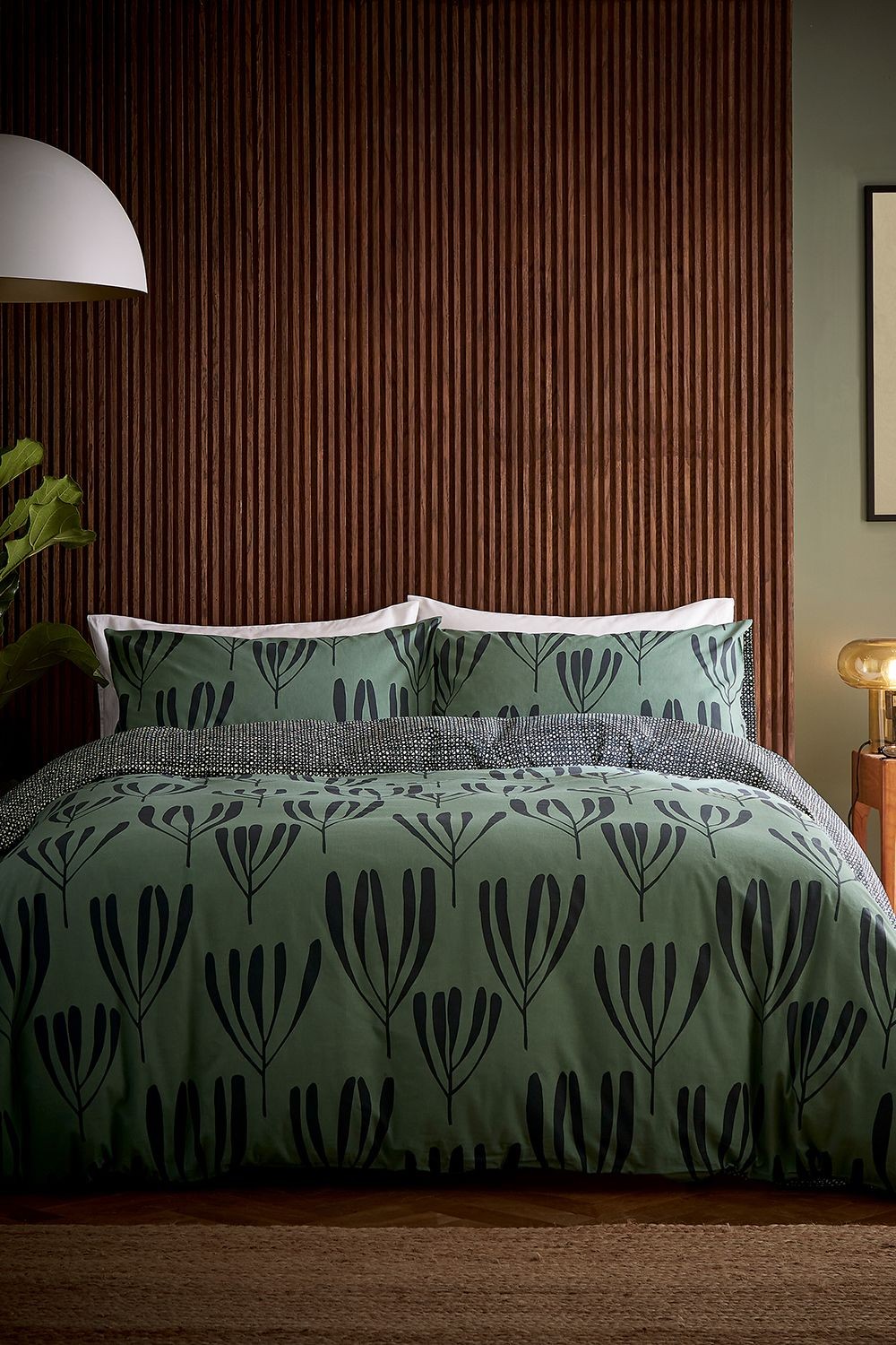 Green cotton duvet cover set featuring a floral design in black, with matching pillowcases, styled on a bed against a textured wooden wall. Size: King.