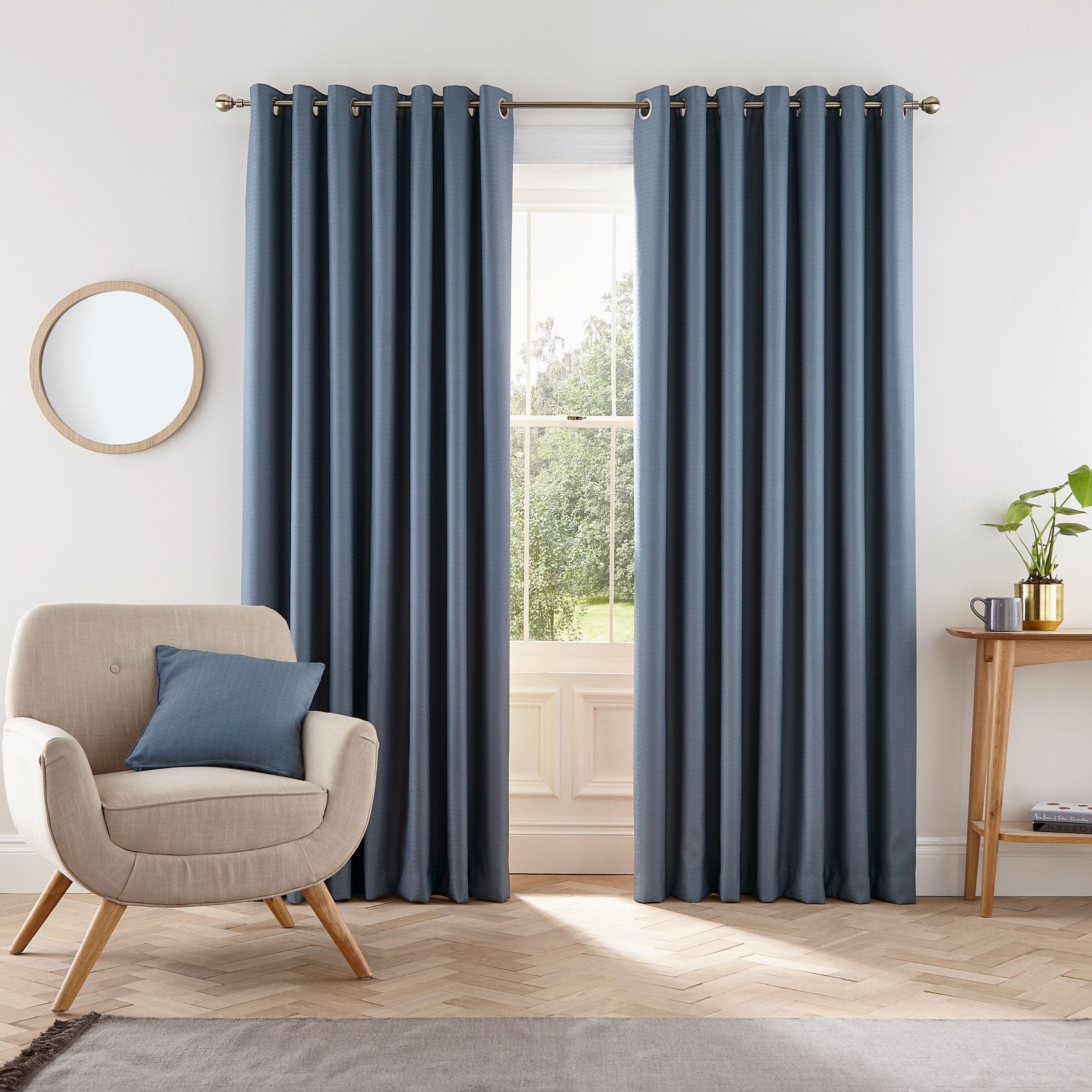 Blue lined curtains with a textured finish, measuring 66" x 54", hang from a silver grommet rod, complementing a cozy room with a chair and a small table.