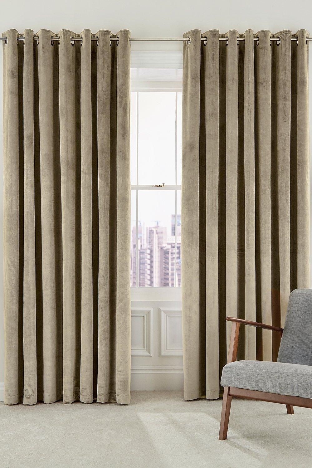 Woven lined curtains in a soft taupe color, featuring a luxurious velvet texture and silver eyelets, elegantly draping beside a window with a city view.