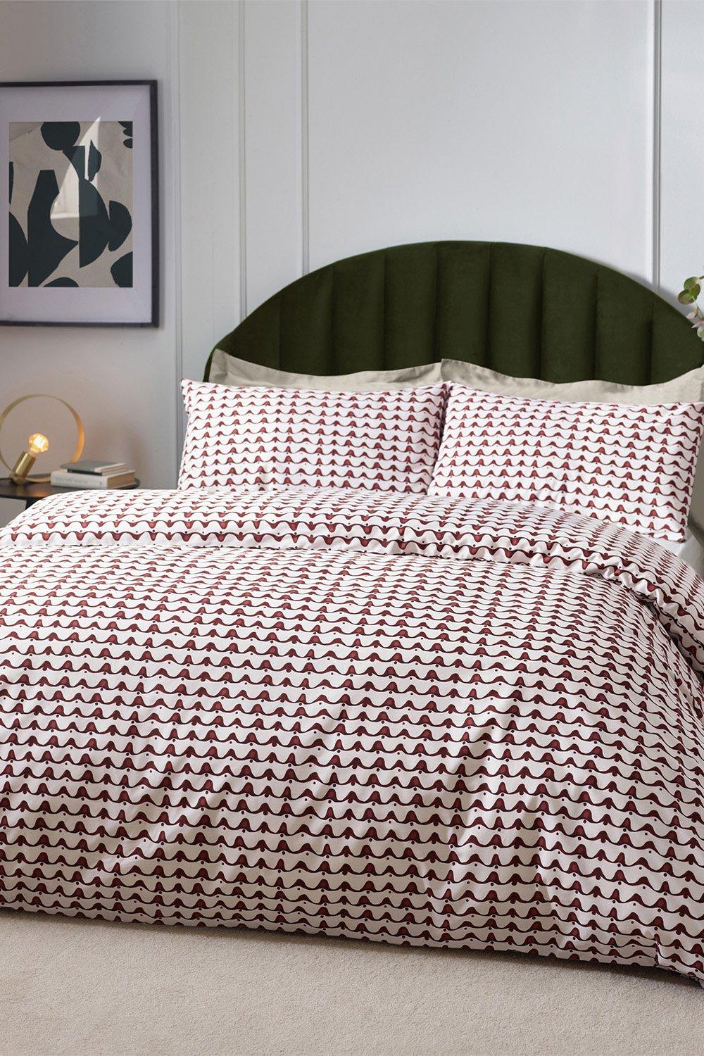 Chestnut red abstract pattern duvet set made of cotton-rich material, featuring matching pillowcases, styled on a green upholstered headboard against a neutral backdrop.