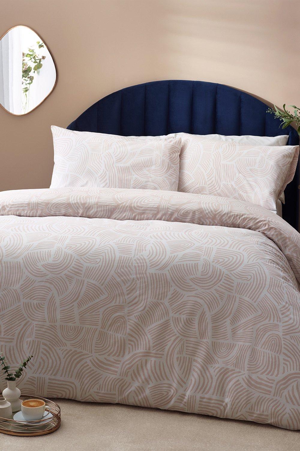 Beige reversible duvet cover set with abstract pattern, made of cotton-rich material, includes two matching pillowcases, styled on a navy upholstered headboard.