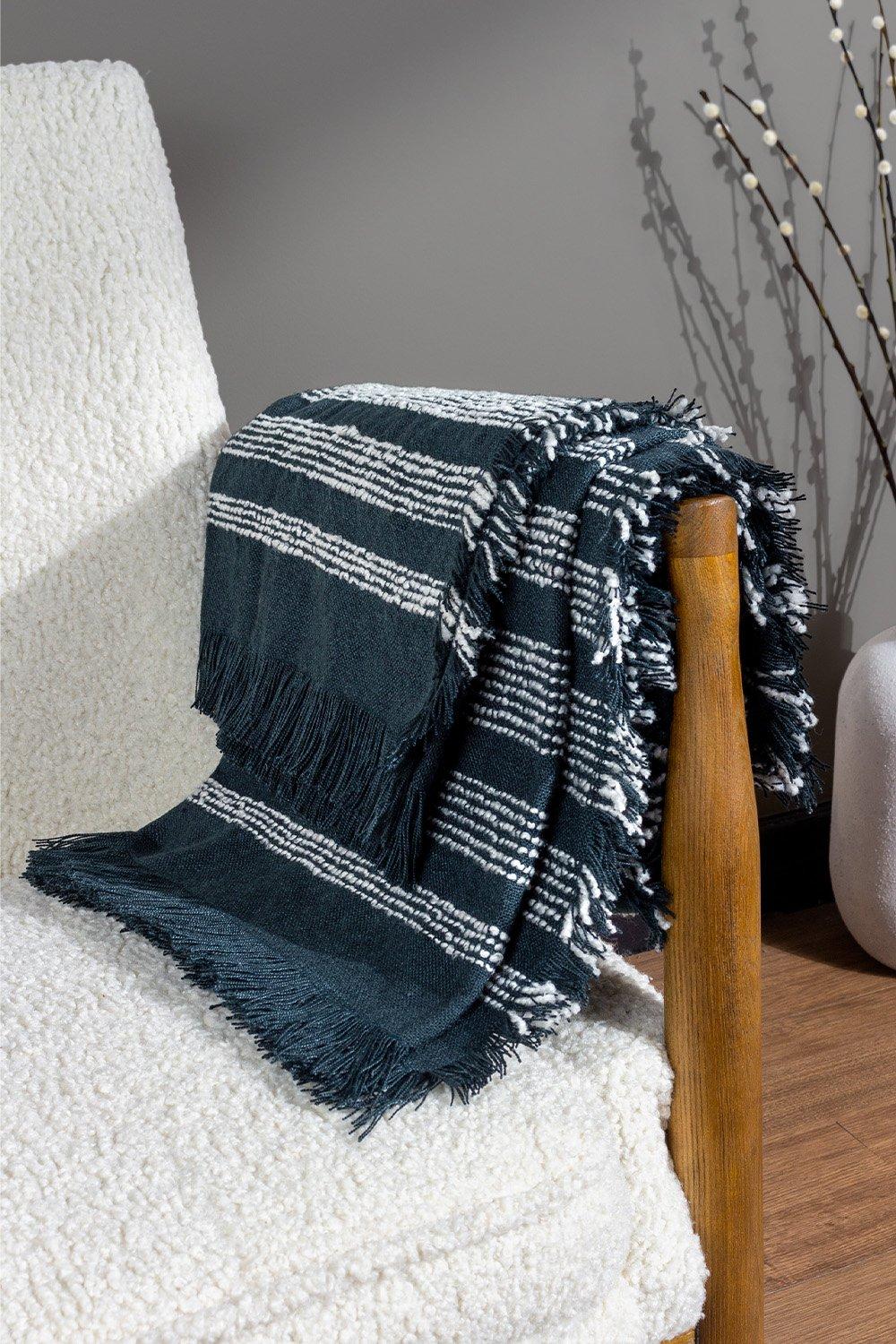 Woven blue throw with white stripes and fringed edges draped over a wooden chair, featuring a soft texture suitable for cozy decor.