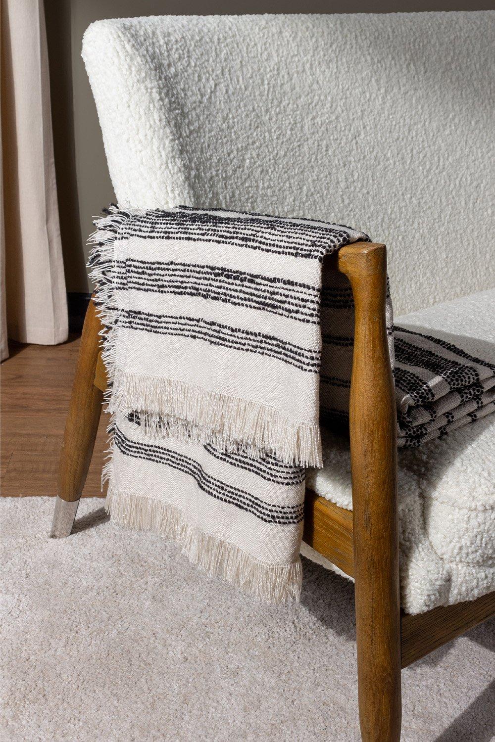 Natural woven throw with black stripes and fringed edges, draped over a wooden chair, showcasing a cozy texture and neutral color palette.