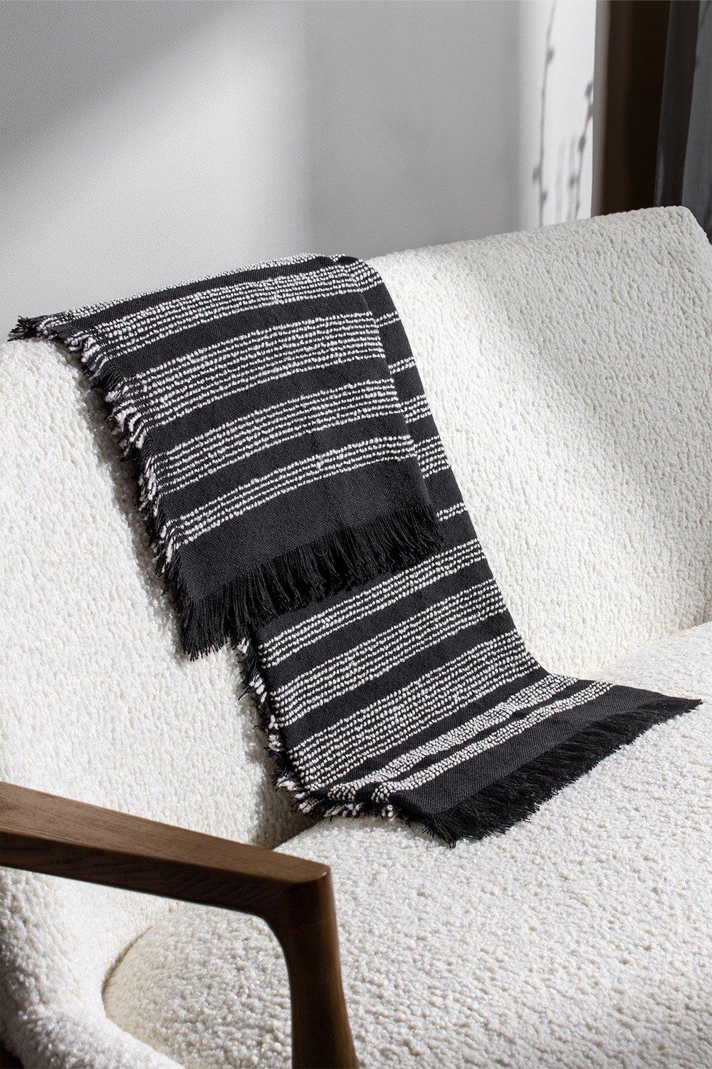 Black and white striped woven throw with fringe edges, made of soft material, draped over a textured cream-colored sofa.