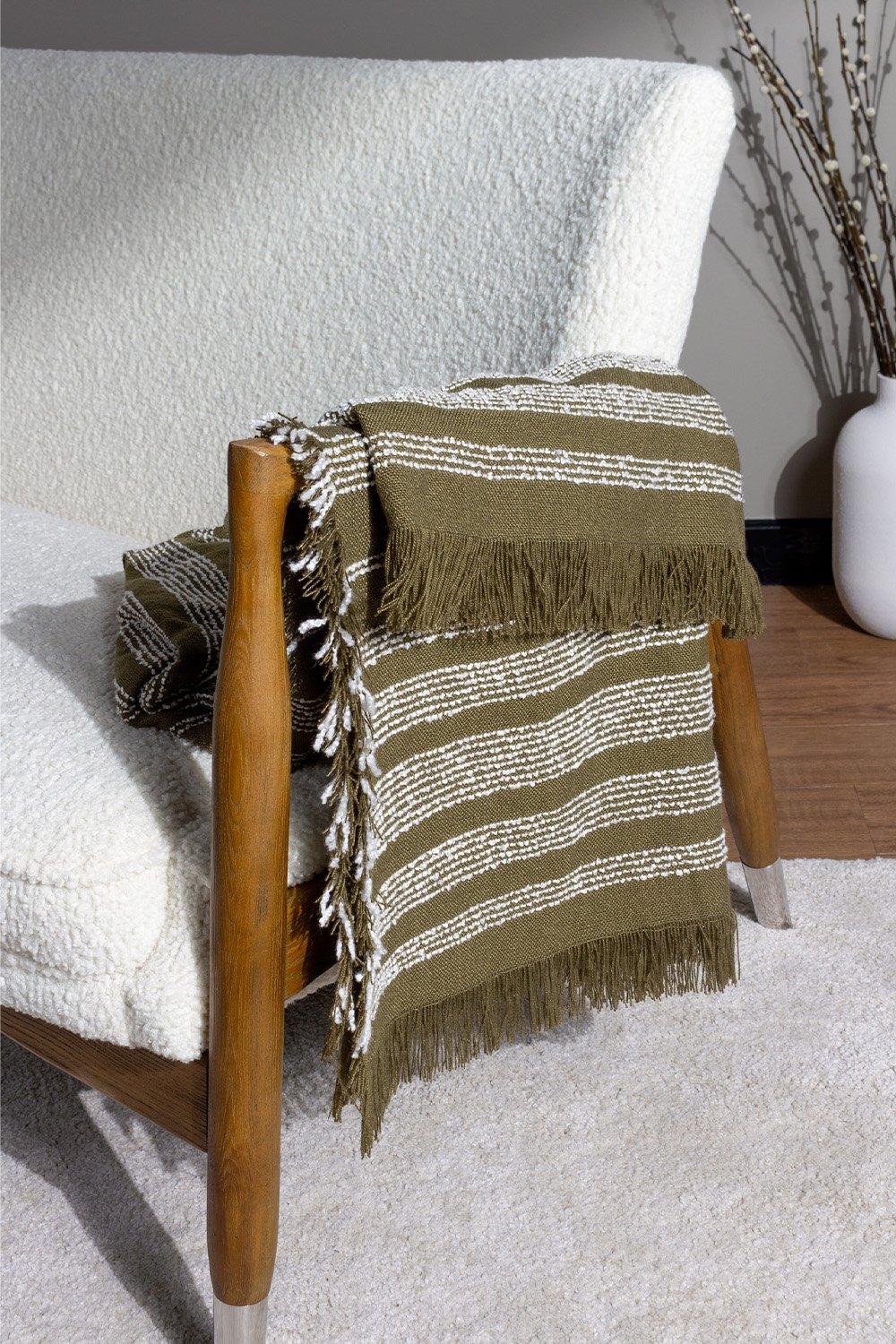 Olive green woven throw with white stripes and fringed edges, draped over a wooden chair, showcasing a soft texture and cozy design.