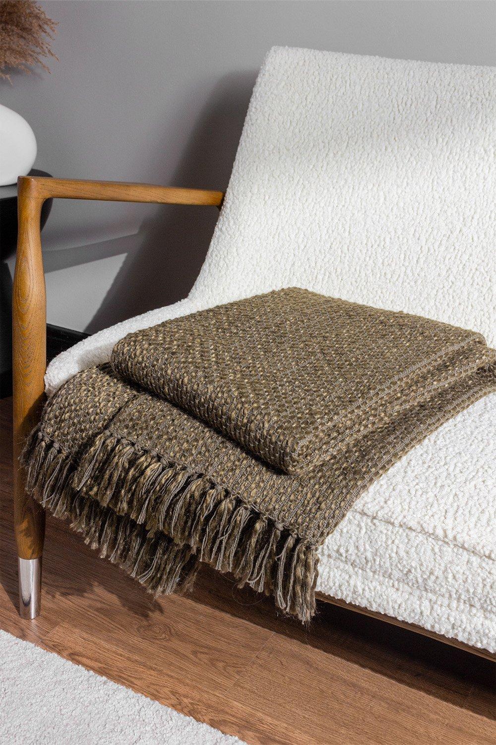 Brown woven yarn tasselled throw made of polycotton, neatly folded on a textured white chair, showcasing its rich color and fringe detailing.