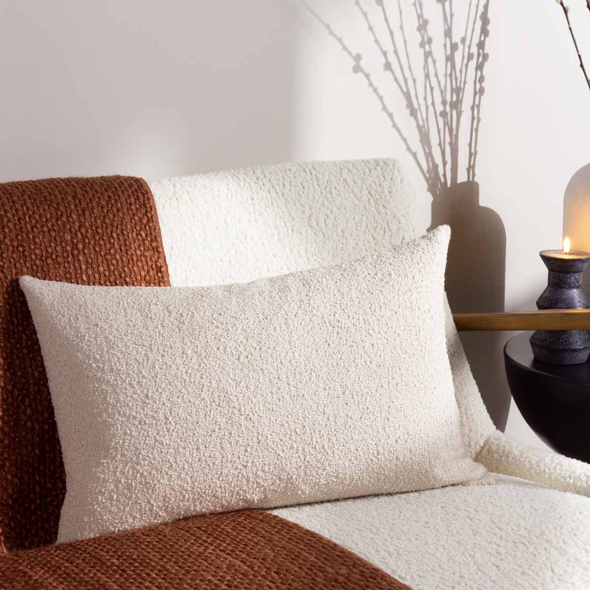 Beige bouclé cushion with a textured surface, rectangular shape, placed on a cozy blanket, featuring soft, neutral tones and a stylish, modern design.