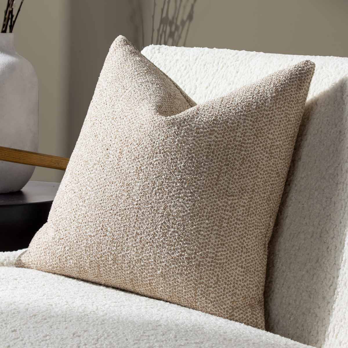 Beige square woven jacquard cushion with a textured surface, featuring a stylish design, placed on a light-colored sofa with a minimalist vase in the background.