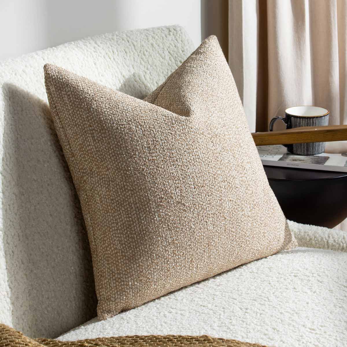 Brown square woven jacquard cushion with a textured surface, featuring a subtle pattern, placed on a cozy white sofa beside a dark side table and a cup.