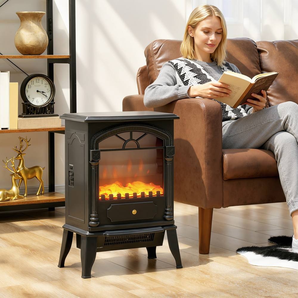 Portable black fireplace with an adjustable thermostat, two heat settings, and a realistic flame effect, placed beside a woman reading on a brown leather sofa.