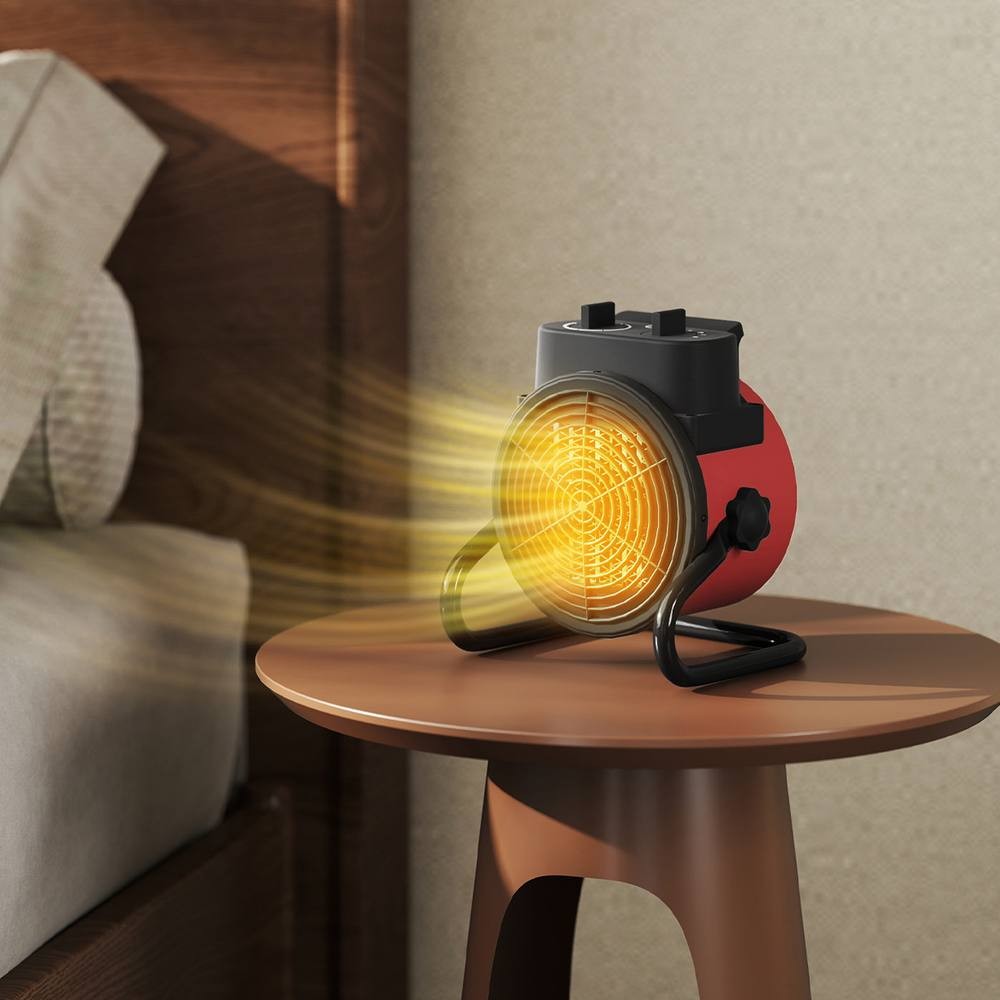 Red ceramic electric heater with a circular grill, portable design, fan feature, and a sturdy base, positioned on a wooden table next to a bed.