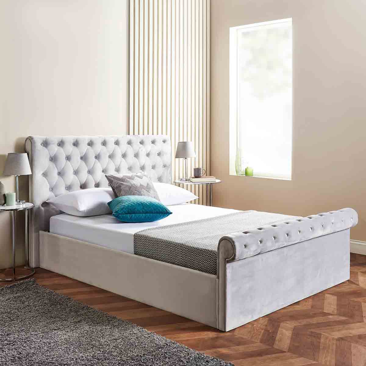 King size ottoman bed in brushed grey velvet with a tufted headboard, featuring a side lift storage compartment and a sleek sleigh design, complemented by decorative pillows.