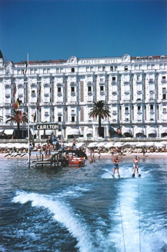 Vibrant canvas print featuring the Carlton Hotel, with clear blue skies, a sandy beach, and people enjoying water sports in the foreground, capturing a lively summer scene.