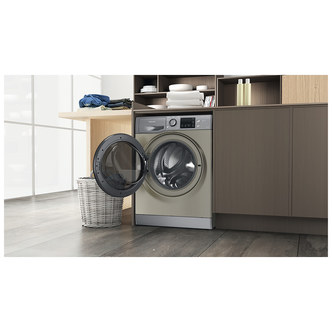 Graphite-colored Hotpoint Futura washer dryer with a transparent front door, featuring a control panel on top and placed beside a wooden countertop and a woven laundry basket.