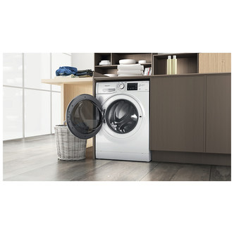 White Hotpoint washer dryer with a transparent door, 9kg wash and 6kg dry capacity, set in a modern kitchen with wooden cabinets and a laundry basket nearby.