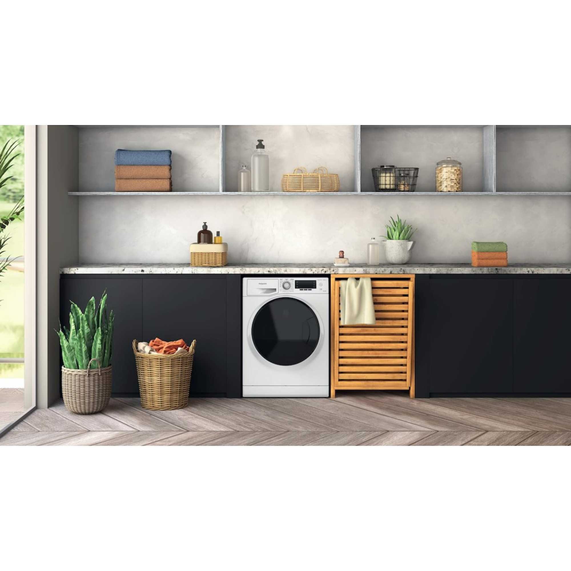 White Hotpoint washer dryer with a black door, featuring a digital control panel, placed in a modern kitchen setting with wooden shelves and decorative storage.
