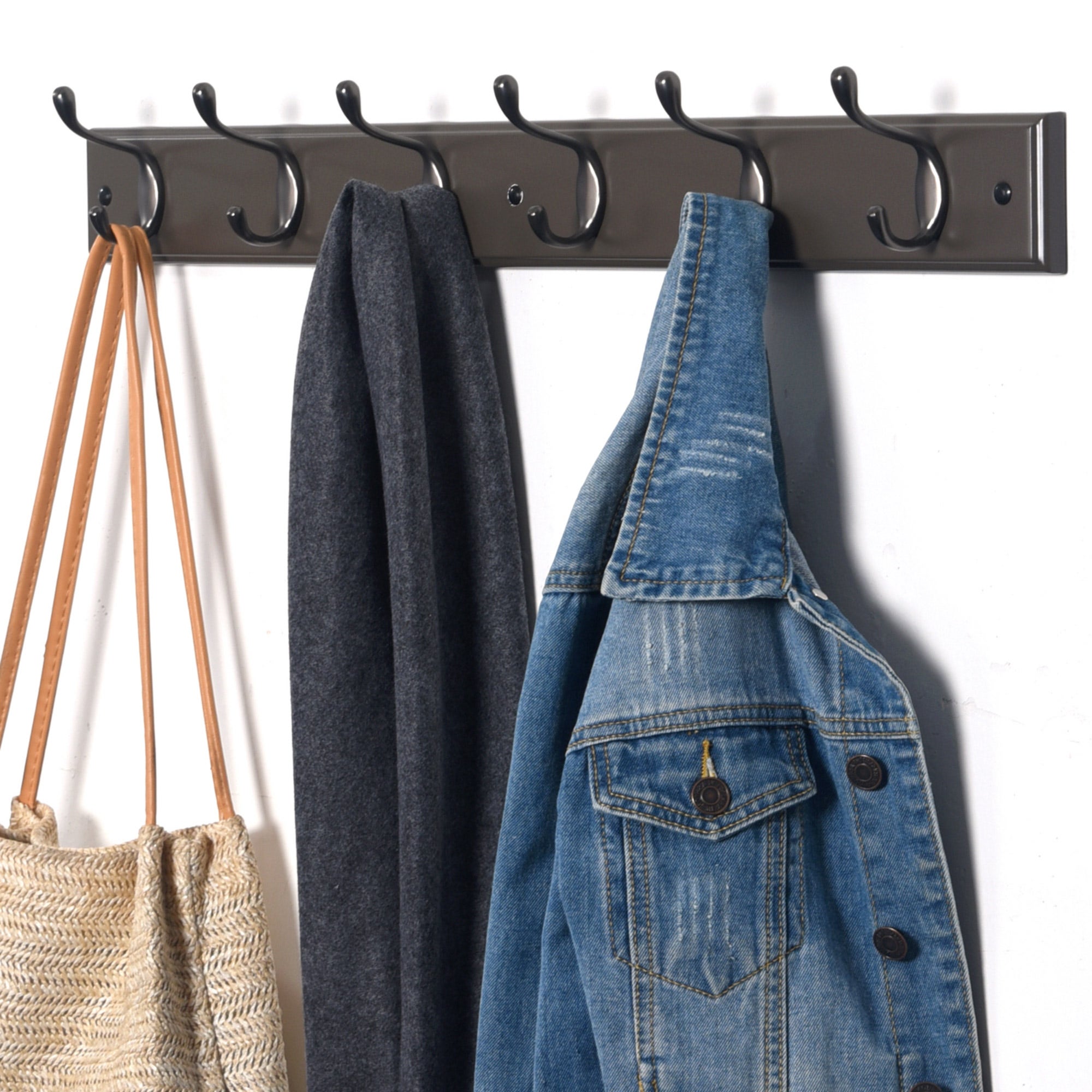 Black wall-mounted coat rack with six double hooks, featuring a wooden base and a sleek design, holding a denim jacket, a grey scarf, and a woven bag.