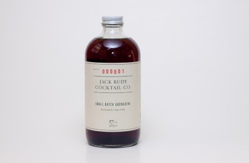 Clear glass bottle filled with deep red grenadine, featuring a simple label with black text that reads "Jack Rudy Cocktail Co. Small Batch Grenadine" and a white background.