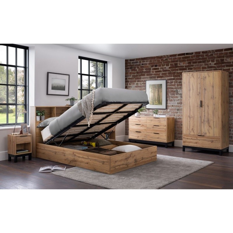 Light oak double bedframe with an ottoman storage feature, featuring a lifted mattress, set against a rustic brick wall, complemented by matching wooden furniture.