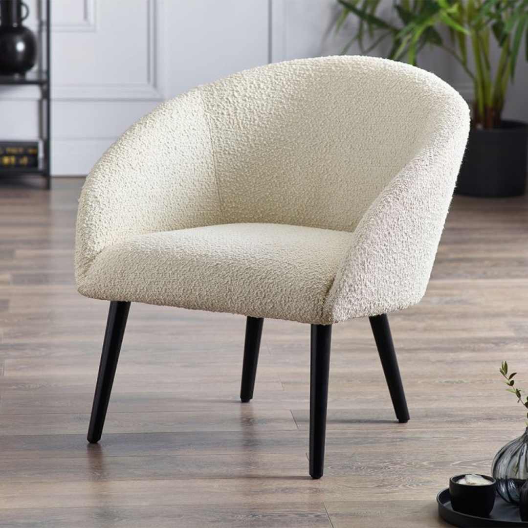 Ivory boucle accent chair with a curved backrest and plush seat, supported by sleek black wooden legs, set against a modern interior backdrop.