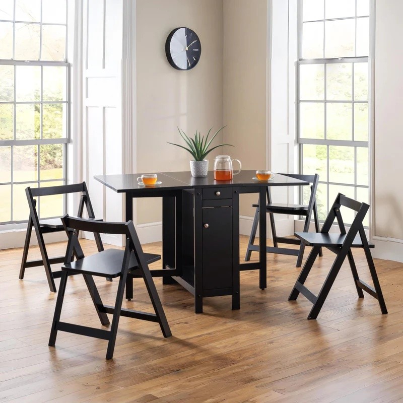 Black wooden dining set featuring a square table with a drawer, surrounded by four folding chairs, set in a bright room with large windows and a clock on the wall.