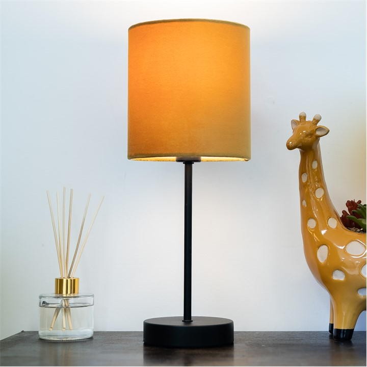 K Living Hove Table Lamp features a cylindrical ochre shade in yellow, a sleek black metal base, alongside a glass diffuser and a decorative giraffe figurine.