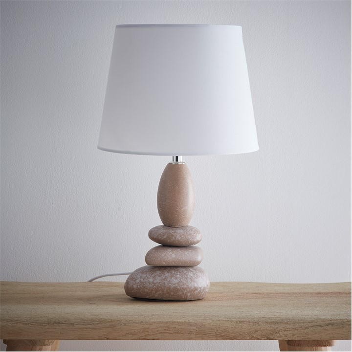 Beige ceramic pebble table lamp with a white shade, featuring a stacked pebble design on a wooden surface.