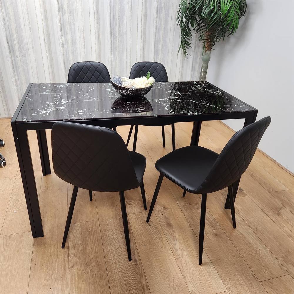 Black glass dining table with a marble effect top, paired with four black gem-patterned chairs featuring quilted upholstery and slender black legs, set against a light wooden floor.
