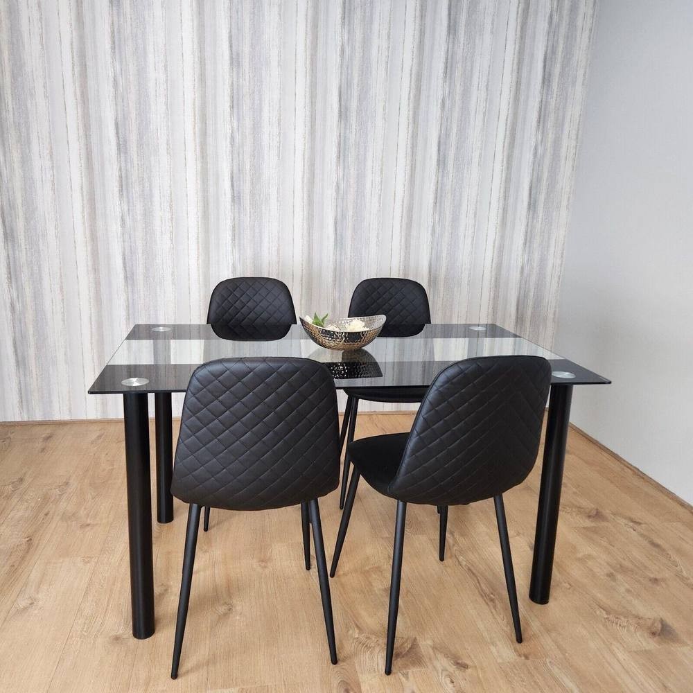 Kosy Koala dining table set featuring a clear glass top with black metal legs, accompanied by four black quilted chairs, all set against a light wood floor and striped wall.