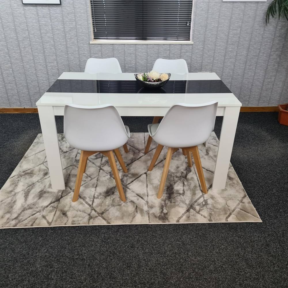 Modern white dining table with a black glass top, accompanied by four white chairs with wooden legs, set on a patterned rug in a stylish interior.