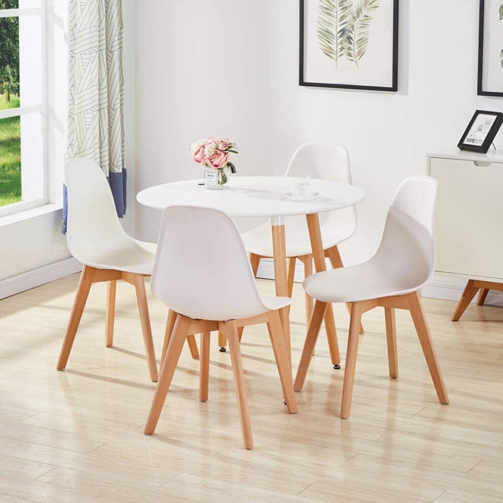 Round white wood dining table surrounded by four white plastic leather chairs with wooden legs, set in a bright room with natural light and decorative wall art.