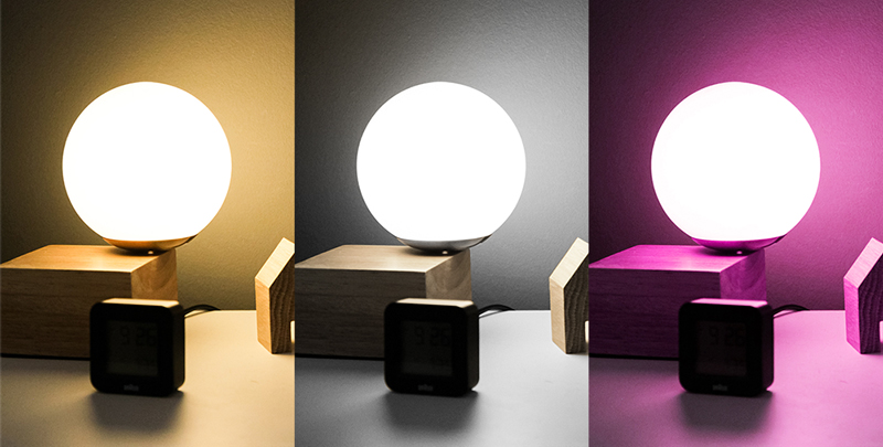 LogiLink WiFi Smart E27 R63 Reflector Bulb with a round, white glass exterior, displayed in three color settings: warm yellow, cool white, and vibrant purple, on a wooden base.